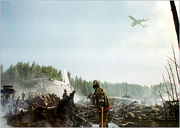 Russian emergency workers stop to look at a passing plane while sifting through the wreckage of a Russian Ilyushin Il-86 passenger plane belonging to Pulkovo Airline that crashed on take-off from Moscow's Sheremetyevo airport July 28, 2002. Russian air police said on Sunday that two people had survived out of 16 crew on board the plane that was bound for St Petersburg on a technical flight carrying the staff home. REUTERS/Stringer