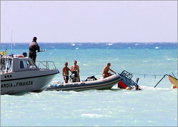 Italian coastguard examine the broken remains of a ship which capsized and sank near Porto Empedolce on the southern island of Sicily September 15, 2002. Thirteen people, including a teenage girl, died when a boatload of illegal Liberian immigrants capsized off the southern coast of Sicily. The 10-metre vessell sank in shallow waters about 200 metres (650 feet) from the shore in relatively calm seas in the early hours of Sunday morning. REUTERS/Tony Gentile