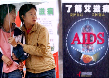 Young Chinese women brave the rain to visit an exhibition on AIDS in Guangzhou, the capital of China's Guangdong province, December 1, 2002. China, long criticised for ignoring a potential explosion of the scourge, announced on Sunday it would send one million students into the countryside over the next year to spread the word about HIV/AIDS prevention and convince people not to discriminate against sufferers. REUTERS/China Photo