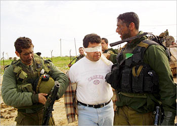 Israeli troops take Reuters television cameraman Ahmed al-Khatib (C) into custody at the Erez crossing at the Gaza Strip border February 23, 2003. The Israeli army detained the Palestinian cameraman on Sunday, drawing a written protest from the international mediaorganisation demanding his immediate release. The army said it suspected the 34-year old journalist was involved in "terrorist activities". Khatib was led away while he was filming in Beit Hanoun, a town in northern Gaza where Israeli forces fought fierce battles with Palestinian gunmen after entering it shortly after midnight. Khatib dismissed the army accusation. (ISRAEL OUT) (NO ARCHIVE) ( NO SALES) ( EDITORIAL USE ONLY) REUTERS/Dani Shalamon