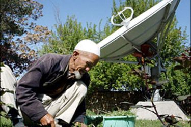 r - A gardener, Koka Abdullah, cuts grass in front of a large satellite dish at a house in Kabul, April 21, 2003