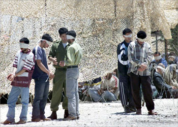 : An Israeli soldier takes a group of blindfolded and handcuffed Palestinians into detention at an army camp south of Hebron 24 June 2003, after they were arrested in the West Bank town last night. Israeli troops nabbed 150 suspected Palestinian militants, including 130 from the Islamist movement Hamas, in Hebron alone, in the largest single arrest campaign since the start of the intifada or uprising against Israeli occupation in September 2000.