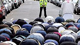 R: A British police officer watches over British Muslims as they gather for Friday prayers outside the Finsbury Park Mosque, London,