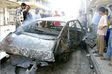 AFP - People look at a destroyed vehicle following a twin motorbike explosion along a main street in the northern city of Mosul 02 June 2005. Five people were killed, including a policeman,