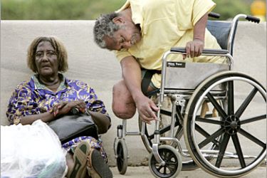 REUTERS /A handicapped man slumps in a wheelchair while a relative sits by after their rescue by boat from floodwaters in New Orleans, September 1, 2005.