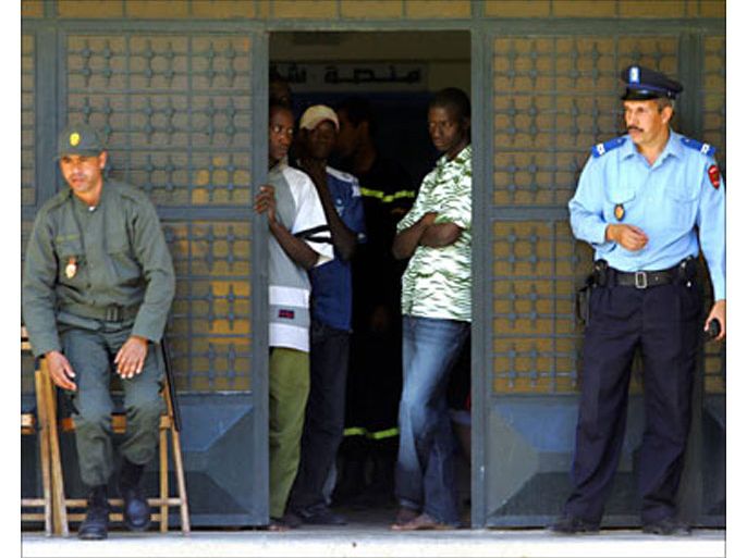 r_Moroccan officials stand as African would-be immigrants look out from the doorway of a camp in Oujda, in northern Morocco in this October 12, 2005 file photo