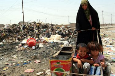 An Iraqi mother wheels her children past a garbage dump in Basra's Hayaniah northern district on April 23, 2008.