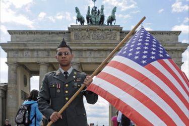 A man dressed as a US soldier holds a US flag as he poses for tourists in front of Berlin's landmark the Brandenburg Gate on July 22, 2008.