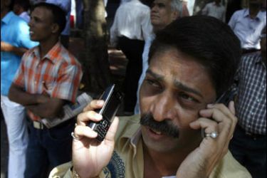 r/A man speaks on his mobile phone as he looks at a screen displaying India's benchmark share index on the facade of the Bombay Stock Exchange building in Mumbai October 24, 2008.