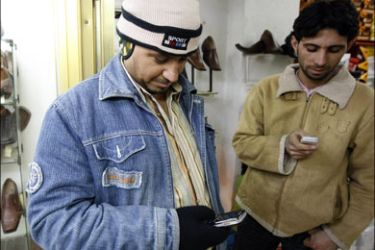 afp : Iraqi shoe shop workers read mobile text messages being circulated playing on the incident last night when an Iraqi journalist threw his shoes at US President George W.