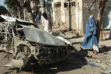 Onlookers are seen next to a mangled wreckage of a car at the site of a suicide car bomb attack in Herat on September 4, 2009. A suicide car bomb attack ripped through an Afghan