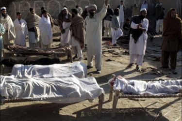 r : Villagers stand beside bodies of blast victims, near the site of a suicide bomb attack, in the town of Lakki Marwat January 2, 2010. Pakistan's government came under renewed