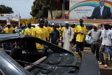 Picture taken on October 22, 2010 shows supporters standing in front of a damaged car at the entrance of the headquarters of the Presidential candidate for the Rally of the Guinean People (RPG) of Alpha Conde in Conakry. The voting was scheduled for October 24, 2010, but was called off by the head of Guinea's Independent National Electoral Commission amid mutual accusations of violence by rival parties. AFP PHOTO / ISSOUF SANOGO
