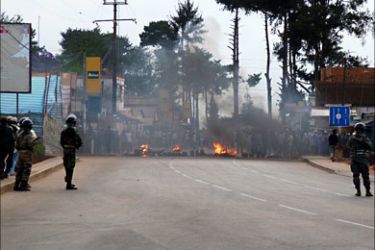 f_Riot police watch a burning barricade on a road on November 17, 2010 in the vicinity of the army barracks where military officers in Madagascar say they have taken over the island