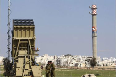 Israeli soldiers stand next to a launcher, part of the Iron Dome rocket shield system, near the southern city of Beersheba, seen in the background, March 27, 2011