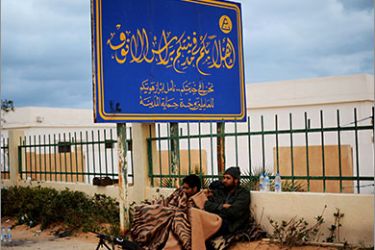 Rebel fighters opposing Libyan ruler Moamer Kadhafi cover themselves with a blanket underneath a sign that welcomes visitors to the north-central Libyan town of Ras Lanuf on March 8, 2011.