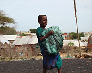 طفلة صومالية تصارع لنقل حمولتها في أحد أحياء كيسمايو (الجزيرة نت) 