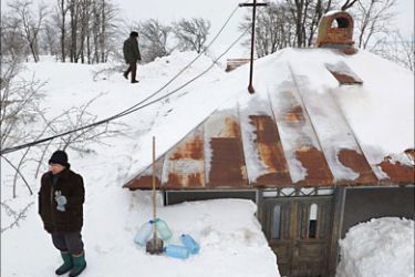 People walk on snow sourrounding a house in the Carligu Mic village, 100km east from Bucharest, on February 11, 2012.