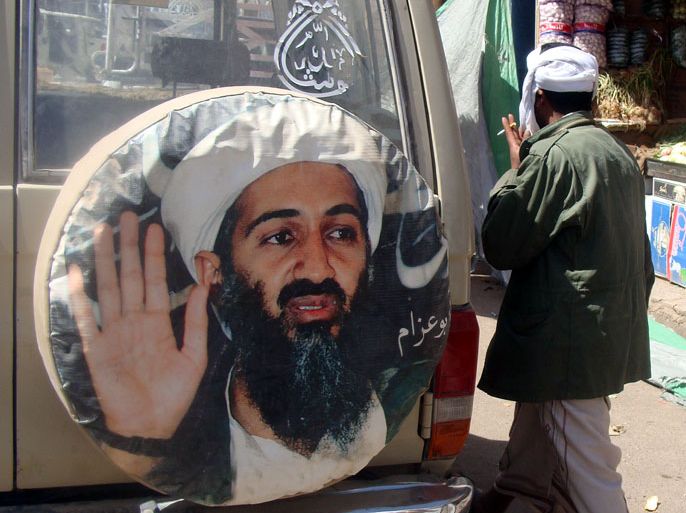 epa03071314 An al-Qaeda-linked fighter walks past a poster of the late head of al-Qaeda Osama bin Laden, while patrolling at a street in the southeast town of Rada, Yemen, 21 January 2012. According to media sources, Yemeni tribal forces in the town of Rada have prevented al-Qaeda-linked fighters from pressing into the town. The al-Qaeda fighters, who seized the town of Rada a week ago, demanded the release of 15 militants from Yemeni prisons before they could withdraw. EPA/STRINGER