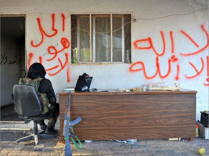 A gunman who said he is a member of a Jihadist group called Shura Taliban Islam sits next to graffiti reading "There's no God but God" (R) and "The solution is Islam" near the Bab al-Hawa border gate between Turkey and Syria on July 21, 2012. Heavy clashes raged between Syrian troops and rebels, with at least 24 people killed nationwide, as the clock ticked down on a 30-day "final" extension of a troubled UN observer mission. AFP PHOTO / BULENT KILIC