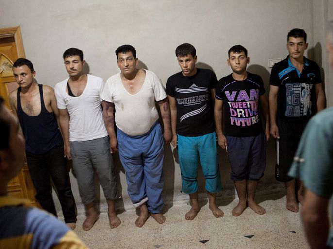 Detainees stand in front of rebels, who say they captured them when they ambushed a military car on the highway from Aleppo to Damascus, at an unknown location the village of Kfar Nubul in Idlib province on July 11, 2012.