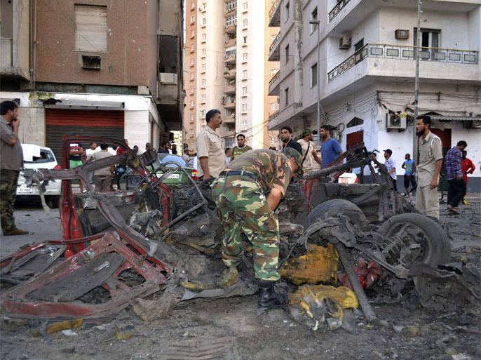 Members of the military and bystanders look at debris after a car bomb exploded near the offices of the military police in Tripoli