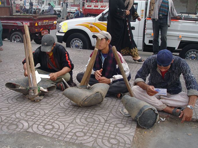 بعض الشباب من عمال اليومية يجلسون على الرصيف في انتظار من يطلبهم لأداء عمل يومي