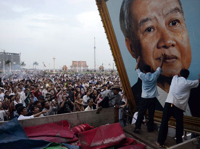 Cambodian people watch as workers install a portrait of the late former king Norodom Sihanouk in front of the Royal Palace in Phnom Penh on October 16, 2012. Grieving Cambodians wore black ribbons and flags flew at half-mast on October 16 as the nation mourned the death of revered ex-king Norodom Sihanouk and prepared for the return of his body from China. AFP PHOTO/TANG CHHIN