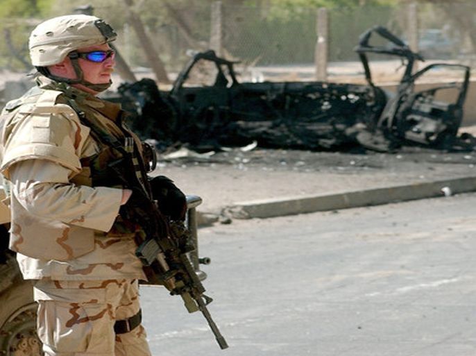 epa000276188 A US soldier stands guard near the remains of a burnt-out car after a roadside bomb in Baghdad, Iraq on Thursday, 16 September 2004. One civilian was injured in the explosion which targeted a car carrying foreigners working for KBR, a subsidiary of Halliburton. No one from KBR was injured. EPA/ALI ABBAS