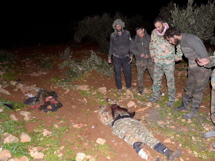 جنود نظاميون ينظرون لجثتيْ مقاتلين سقطا في معركة بتل حاصل في حلب (الفرنسية)