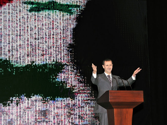 العلم السوري خلف الأسد وقد رسمت عليه وجوه مئات القتلى الحكوميين (الفرنسية)