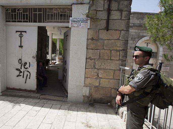 An Israeli border guard stands next to anti-Christian graffiti reading in Hebrew, "Jesus is monkey" that was daubed on the Church of the Dormition, one of Jerusalem's leading pilgrimage sites, early on May 31, 2013. Israeli police said they suspected Jewish religious extremists of spraying the Hebrew-language insults at the site, where tradition says the Virgin Mary died. AFP PHOTO/AHMAD GHARABLI