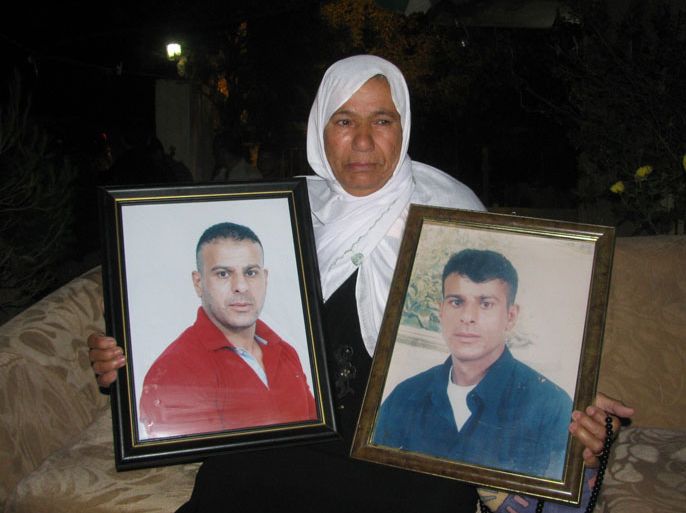 والدة الأسير محمود أبو صالح الذي يعاني من ورم غامض في الرقبة تحمل صورتيه
