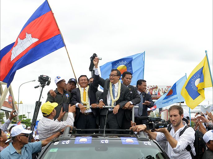 Cambodian opposition leader of the Cambodia National Rescue Party (CNRP) Sam Rainsy (C) raises his arm with Kem Sokha (center L) Vice president of the Cambodia National Rescue Party (CNRP) as they greet supporters along a street in Phnom Penh on July 19, 2013. Cambodia's newly pardoned opposition leader arrived home from exile on July 19, to help his party's bid to end Prime Minister Hun Sen's nearly three decades in power, his party said. AFP PHOTO/ TANG CHHIN SOTHY