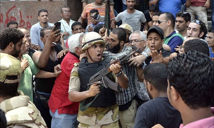 An army officer points his weapon at the crowd as he helps an Islamist man to leave Cairo's Al-Fath mosque where Islamist supporters of ousted president Mohamed Morsi hole up on August 17, 2013. The standoff at al-Fath mosque in central Ramses Square began on August 16, with security forces surrounding the building where Islamists were sheltering and trying to convince them to leave. AFP PHOTO / MOHAMED EL-SHAHED