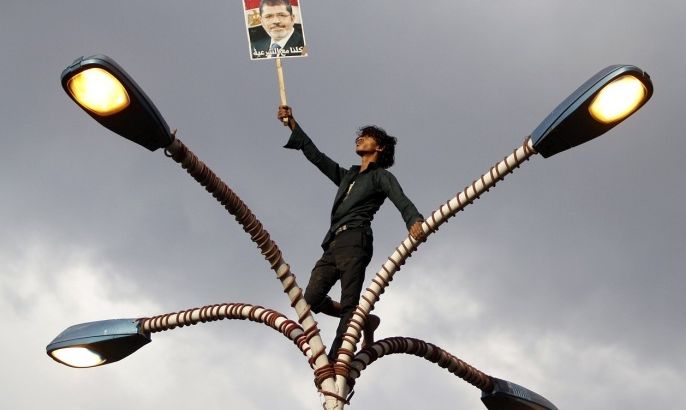 A supporter of deposed Egyptian President Mohamed Mursi holds up his photo while standing at the top of lamp posts during a march to show solidarity with his supporters in Egypt, in Sanaa August 15, 2013. The poster reads "We are all with legitimacy".
