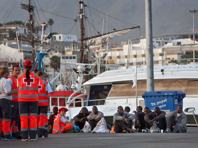 DM001 - Los Cristianos, -, SPAIN : Would-be immigrants wait on the ground next to Red Cross members at Los Cristianos harbour in the Spanish Canary Island of Tenerife, on August 24, 2013. A vessel carrying 26 would-be immigrants was rescued off the coast of the Canary Islands. AFP PHOTO/ DESIREE MARTIN