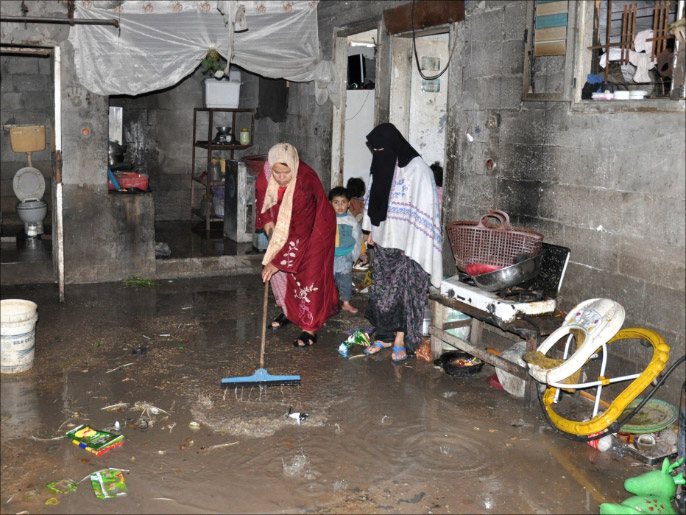مواطنتان من عائلة البيشاوي تحاولان إخراج المياه من المنزل الغارق (الجزيرة)