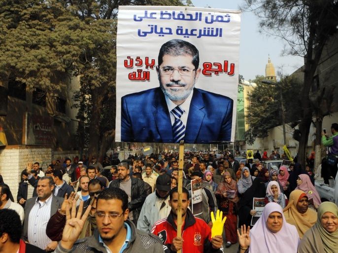 Supporters of Egypt's ousted President Mohammed Morsi hold his poster as they raise their hands with four fingers which has become a symbol of the Rabaah al-Adawiya mosque, where Morsi supporters had held a sit-in for weeks that was violently dispersed in August, during a protest in Cairo, Egypt, Friday, Dec. 20, 2013. Arabic reads, " my life is the cost to defend legitimacy, and Morsi will be back. (AP Photo/Amr Nabil)