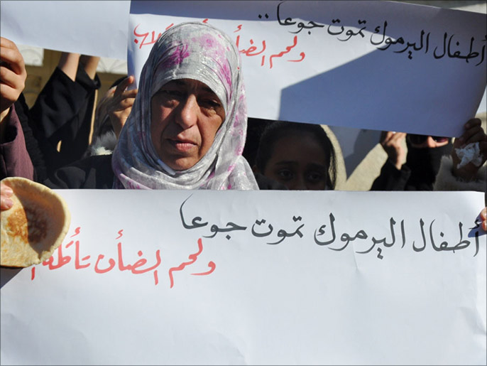 مسنة فلسطينية تحمل رغيف خبز ولافتة تضامنا مع لاجئي اليرموك (الجزيرة)