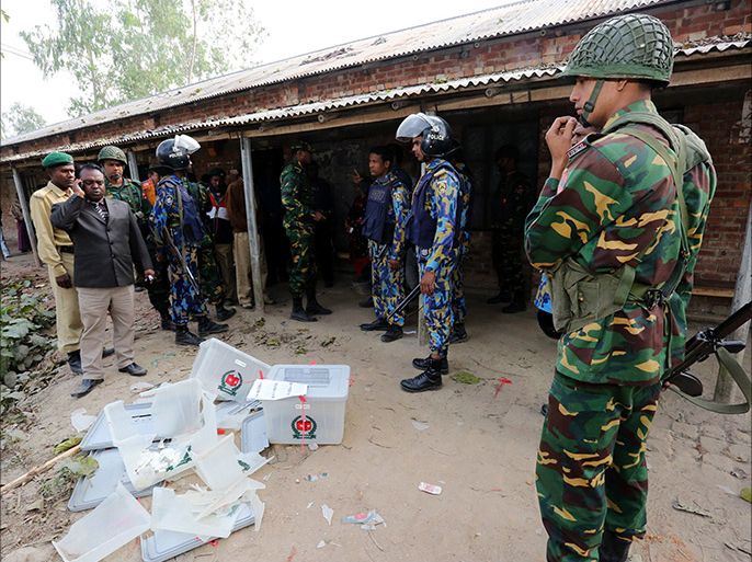 Bangladeshi police and soldiers stand next to damaged ballot boxes in front of a polling station after it was attacked by protestors in the northern town of Bogra on January 5, 2014. Protestors firebombed polling stations and attacked police as Bangladesh went ahead with a violence-plagued election boycotted by the opposition. AFP PHOTO/STR