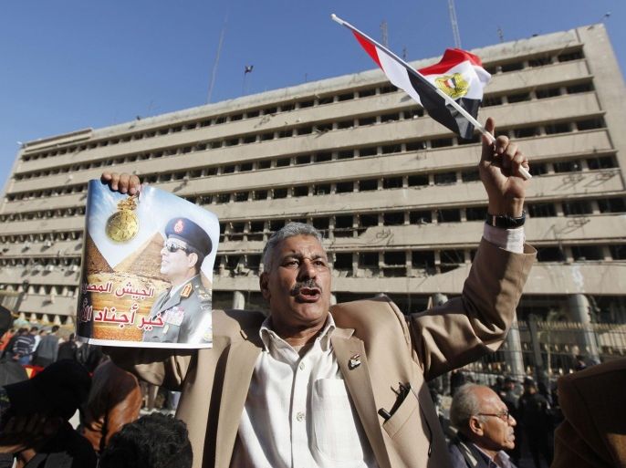 A supporter of Egypt's army chief General Abdel Fattah al-Sisi holds a poster of Sisi in front of the damaged Cairo Security Directorate building, which includes police and state security, after a bomb attack in downtown Cairo, January 24, 2014. A suicide bomber in a car blew himself up in the parking lot of a top security compound in central Cairo on Friday, killing at least four people in one of the most high-profile attacks on the state in months, security sources said. The poster reads "We will die and Egypt will live." REUTERS/Mohamed Abd El Ghany (EGYPT - Tags: POLITICS CIVIL UNREST CRIME LAW)