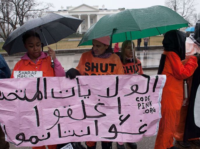 NK009 - Washington, District of Columbia, UNITED STATES : Protestors wear orange detainee jumpsuits and black hoods as they hold a banner in Arabic calling for the closing of the US detention center at Guantanamo naval base in Cuba in front of the White House in Washington on January 11, 2014 to mark the 12th anniversary of the arrival of the first detainees at the controversial jail. Some 155 people are still held at Guantanamo, more than half of them Yemenis. AFP PHOTO/Nicholas KAMM