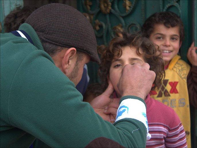 عضو في الفريق الطبي يقوم بتلقيح طفلة في حماة ضد فيروس شلل الأطفال (الجزيرة)