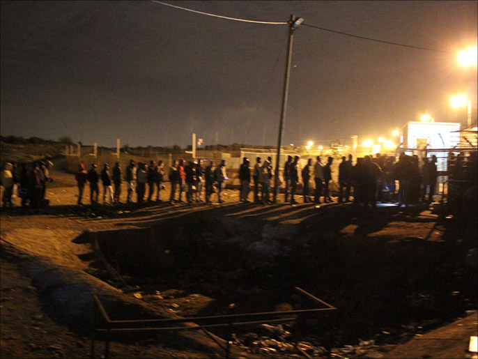 العمال يقفون في طوابير طويلة أمام بوابة المعبر (الجزيرة)