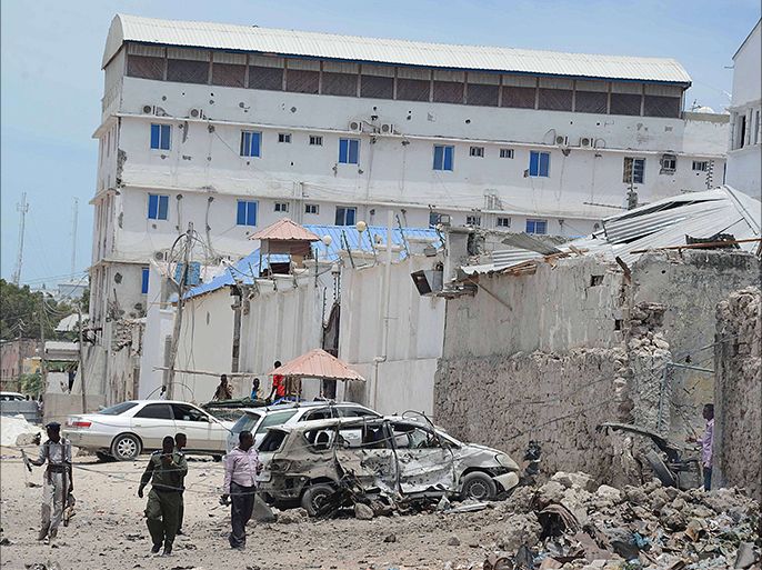 : Somali government soldiers walk around a destroyed car at the site of car bomb blast in front of the Makka Al Mukarrama Hotel in Mogadishu, on March 15, 2014.
