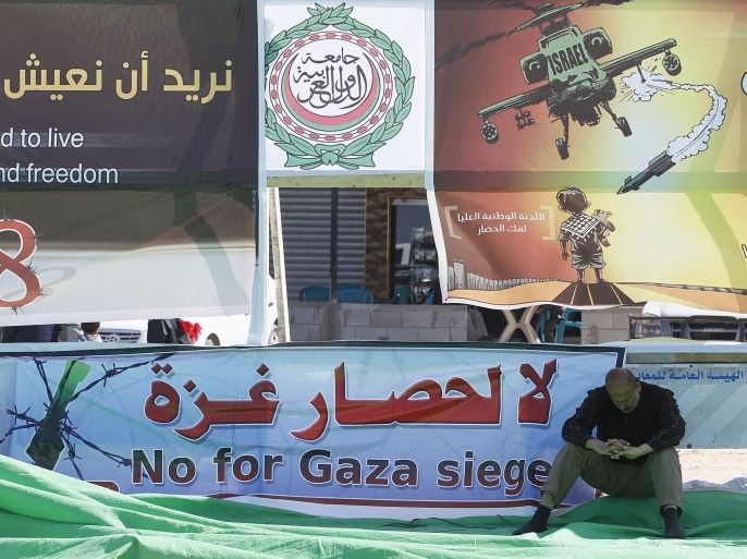 A man sits next to a banner reading in English and Arabic 'No for Gaza siege' at the Rafah border crossing with Egypt in the southern Gaza Strip on February 28, 2014, during a protest to demand that Egypt lift border crossing restrictions. Egypt imposed the restrictions as part of a campaign by its security forces against jihadists in the lawless Sinai Peninsula, which borders Gaza and Israel. AFP PHOTO/ SAID KHATIB