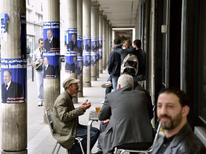 People sit near campaign posters for Algerian president Abdelaziz Bouteflika at a cafe terrasse in a street of the 'Goutte d'Or' district of Paris on April 11, 2014. Long held in suspicion in a largely state-controlled economy, Algerian businessmen are pouring cash into President Abdelaziz Bouteflika's re-election campaign, hoping to benefit from an expected fourth term for the incumbent. By law, candidates are supposed to spend no more than $764,000 (600,000 euros) on their campaign unless the election goes to a second-round runoff. But analysts say the legal limit is set impossibly low for a country which is Africa's largest by area, paving the way for effectively unrestricted spending by the candidates, with the incumbent leading the way. AFP PHOTO / ERIC FEFERBERG