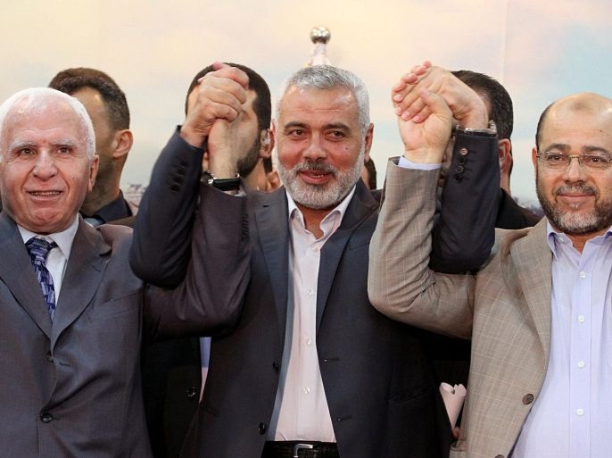 Senior Fatah official Azzam Al Ahmad (L), Hamas Prime minister Sheikh Ismael Haneiya (C) and senior Hamas leader Moussa Abu Marzouk (R) join hands after the announcement of an agreement between the two rival Palestinian groups, in Gaza City, 23 April 2014. Others are not identified. Palestinian rival movements Hamas and Fatah on 23 April agreed to form a unity government and hold general elections. The two rivals have been embroiled in a rift since 2006, after Hamas unexpectedly beat the secular Fatah in parliamentary elections, conducted exactly a year after Mahmoud Abbas won a presidential poll.