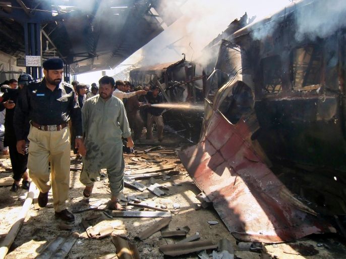A Pakistani police officer investigates as firefighters try to extinguish a burning passenger train following an explosion in Sibi, Pakistan, Tuesday, April 8, 2014. A deadly bomb ripped through a railway car parked at a station in southwestern Pakistan, sending flames and smoke billowing into the air, officials said. (AP Photo/Saleem Gishkori)